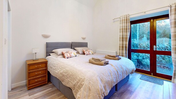Un dormitorio con cama, mesitas de noche, cómoda y ventana con vistas a árboles.