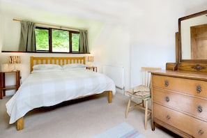 A bedroom with a bed, a dresser, a chair, a window with curtains, and a radiator.