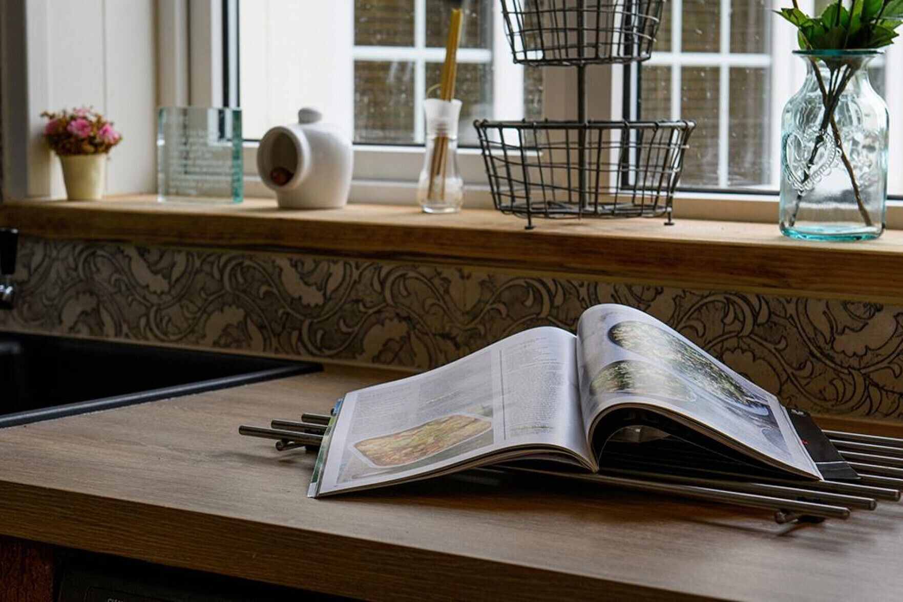 An open book on a wooden surface with a window behind it.