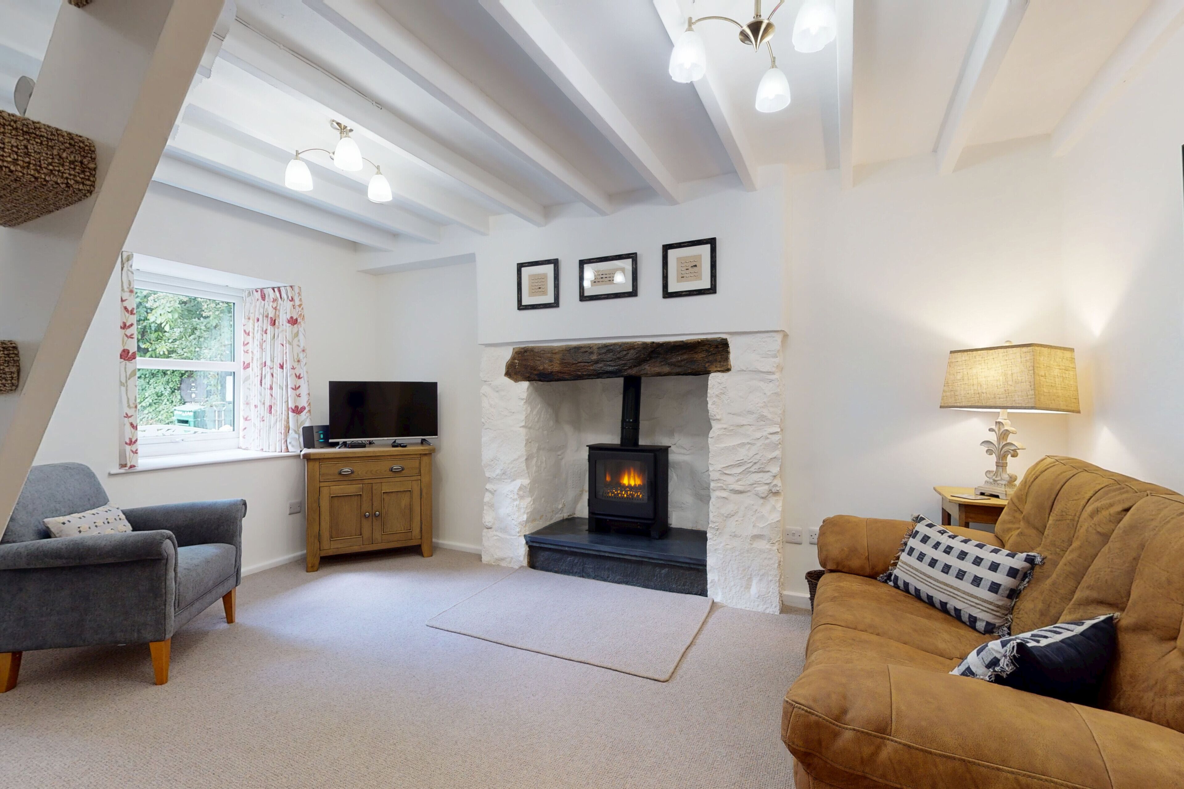A cozy living room with a fireplace, a sofa, a television, and a window with curtains.