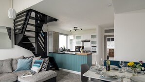 A modern living room with a grey sofa, teal accent wall, and a black spiral staircase. - Rivage - Two Bedroom Cottage, Sleeps 4 (Deganwy)