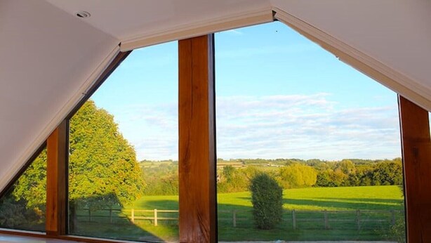 A room with a large triangular skylight overlooking a green landscape. - Amazing views in luxury cottage (Cheltenham)