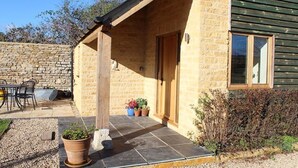 A stone building with a wooden porch, a dining table, and potted plants. - Amazing views in luxury cottage (Cheltenham)