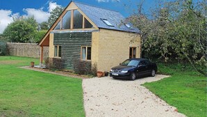 A two-story house with a sloped roof, a car parked in front, and a gravel driveway. - Amazing views in luxury cottage (Cheltenham)