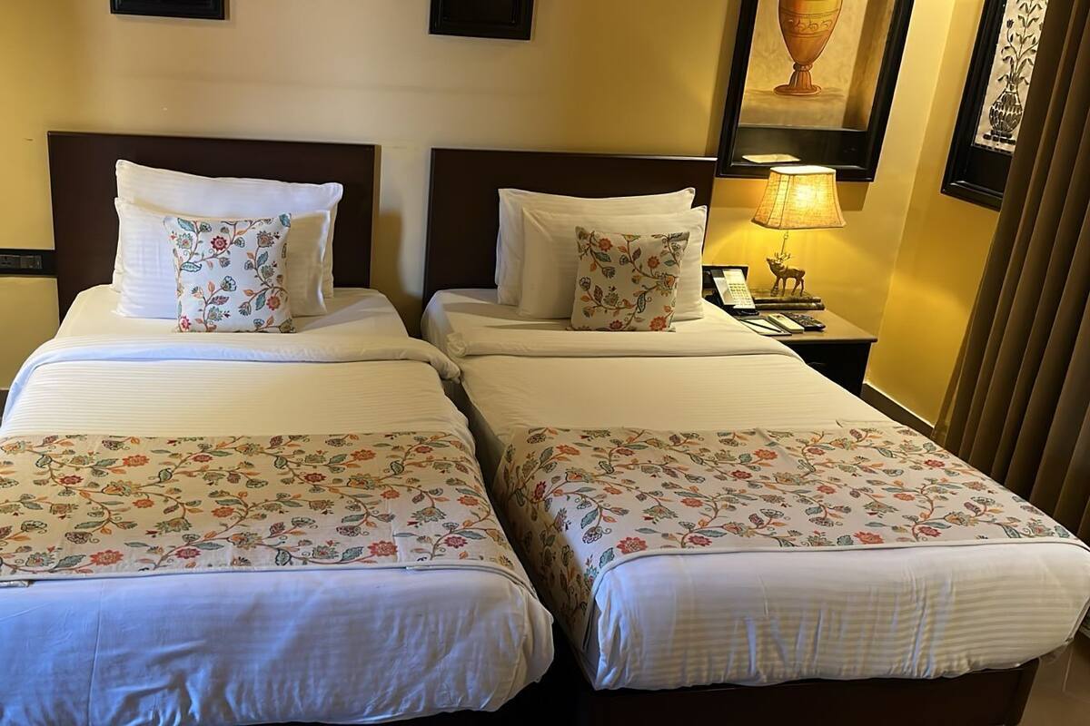 A hotel room with two beds, each with floral-patterned bedspreads and matching pillows. There is a nightstand with a lamp and a phone.
