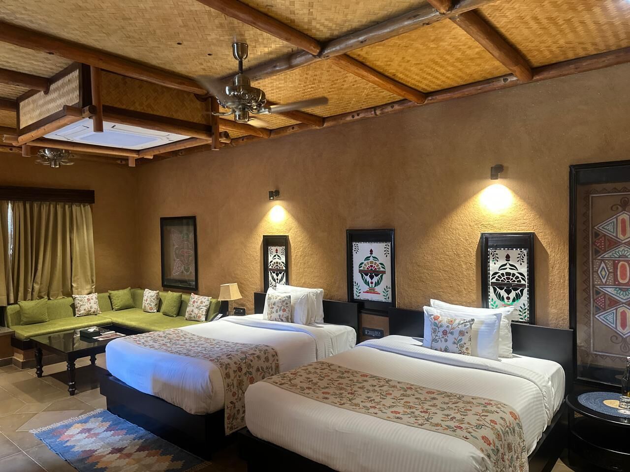 Une chambre d’hôtel avec deux lits, un canapé, une table basse et un ventilateur de plafond.
