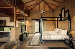 A spacious bedroom with a four-poster bed, a flat-screen TV, a desk, and a balcony view. - Aamaghati Wildlife Resort (Sawai Madhopur)
