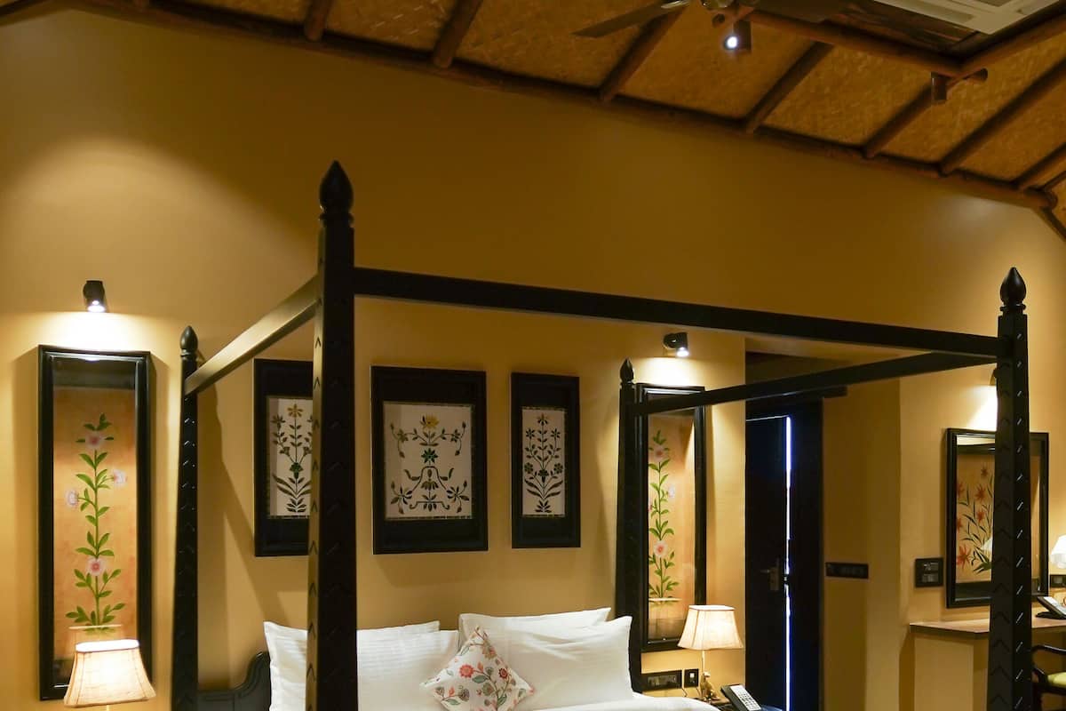 A four-poster bed with white linens, a ceiling fan, and framed botanical prints on the walls.