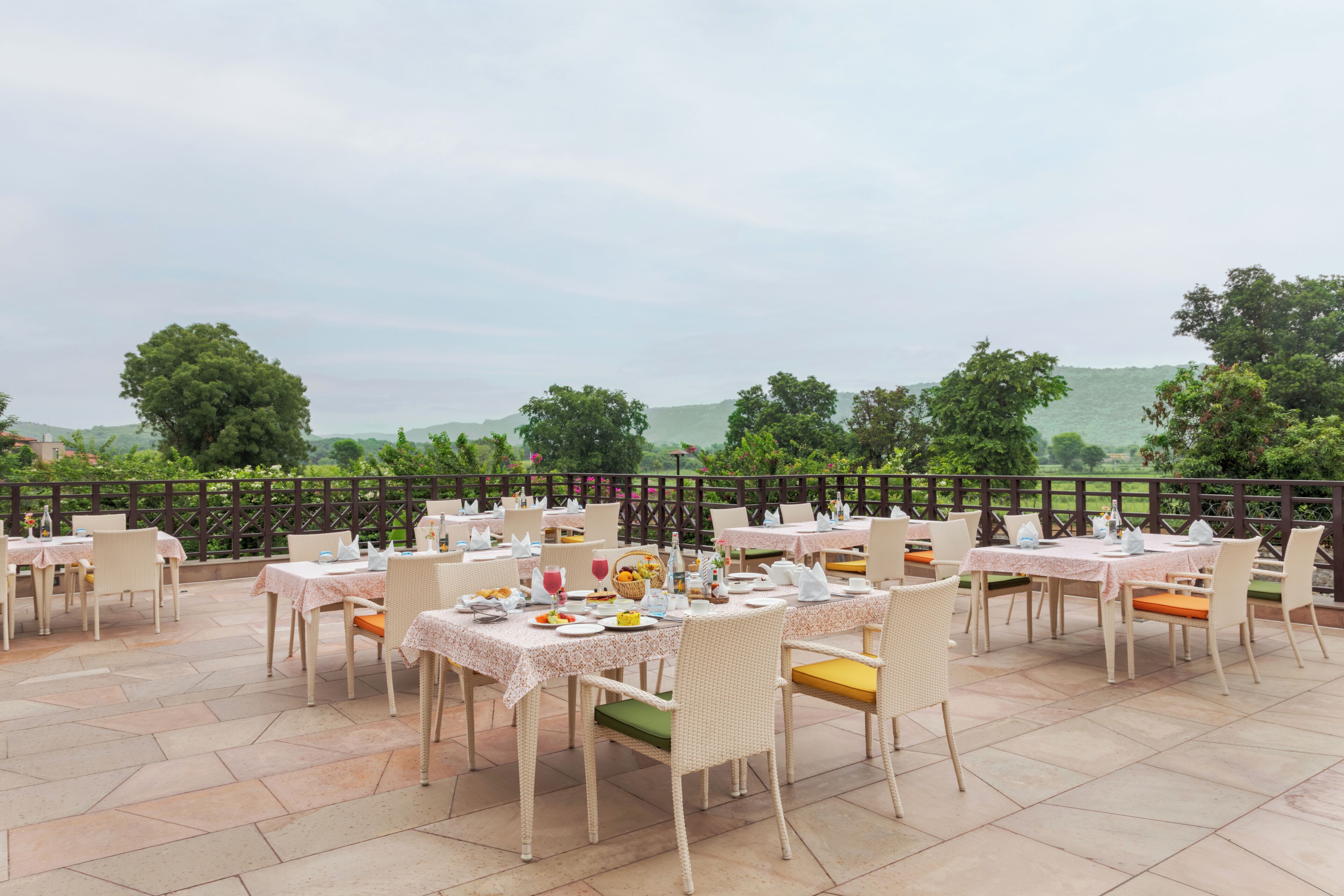 Un espace de restauration en plein air, avec des tables et des chaises, agrémenté d’une végétation luxuriante et dominant des collines.