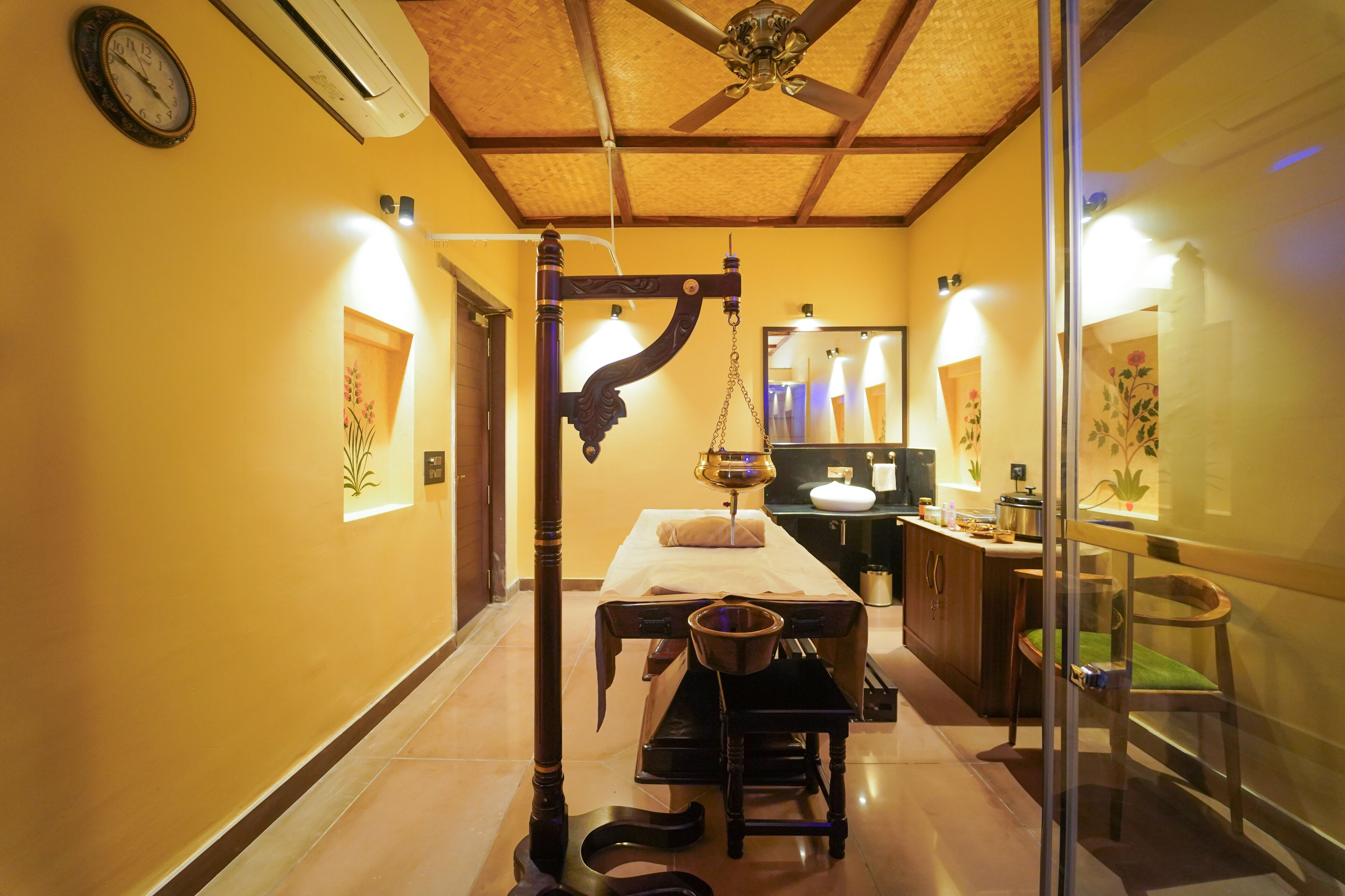 A room with a bed, bedside table, and a small desk with a chair. There is a window with a view of the outside.