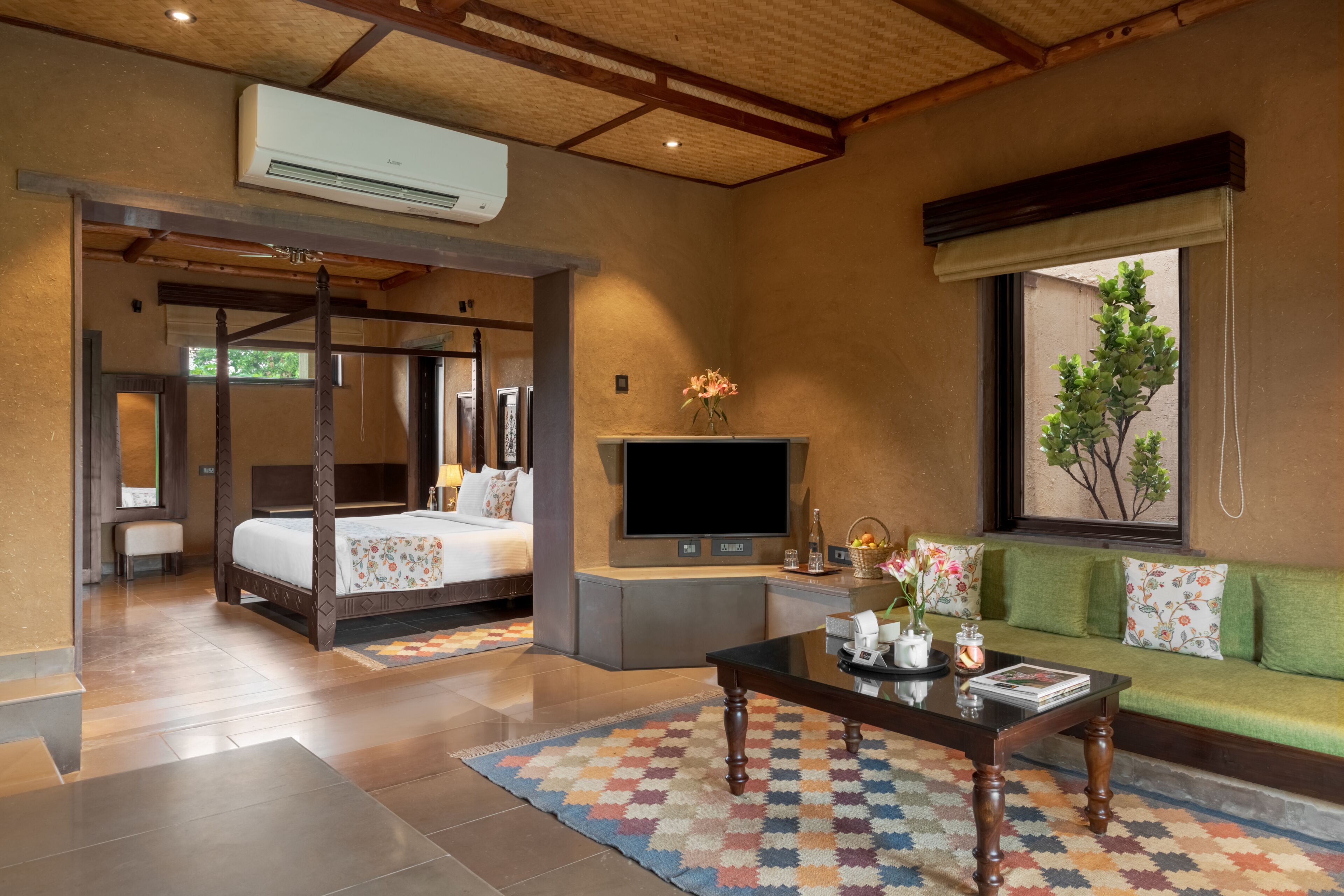 Quarto de hotel com cama, televisão, sofá e janela com vista para o verde.