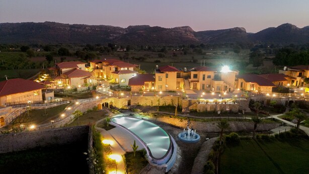A well-lit resort with multiple buildings, a swimming pool, and a fountain. - Aamaghati Wildlife Resort (Sawai Madhopur)