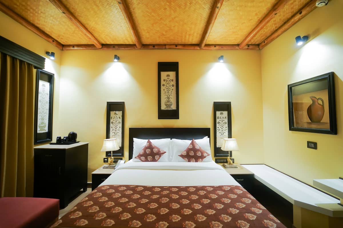 A hotel room with a large bed, two bedside tables with lamps, a wooden ceiling, and framed artwork on the walls.