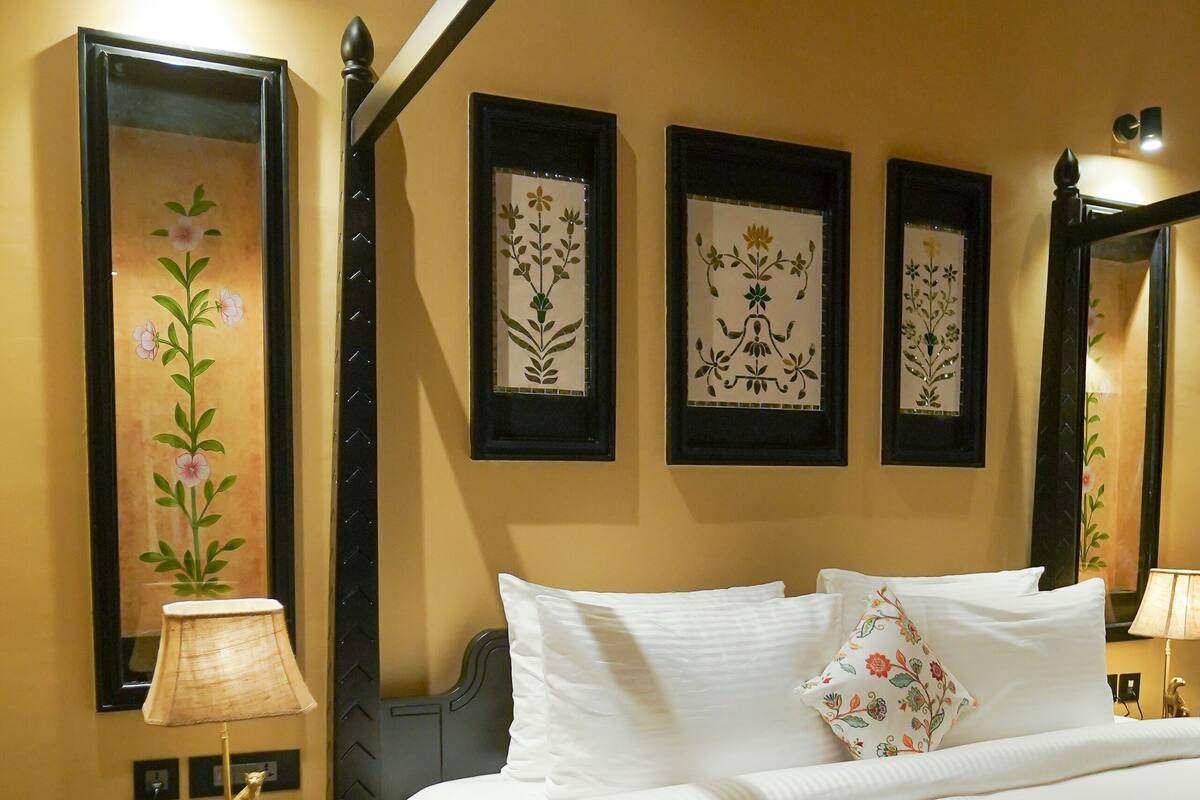 A hotel room with a bed, a nightstand with a lamp, a floral-patterned rug, and three framed wall decorations.