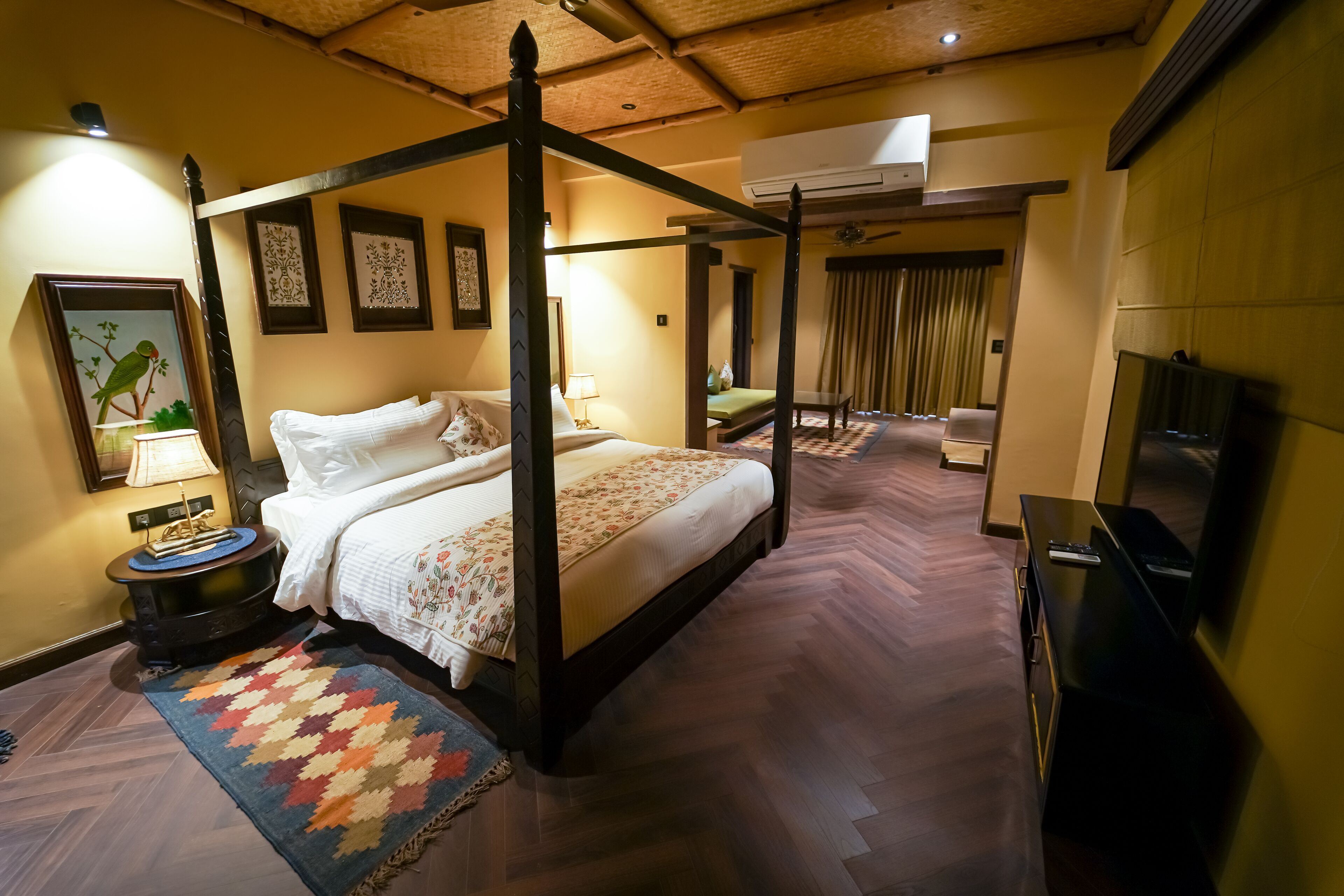 Un lit à baldaquin avec une couvre-lit à motifs floraux, un téléviseur sur le côté droit et un parquet à chevrons.