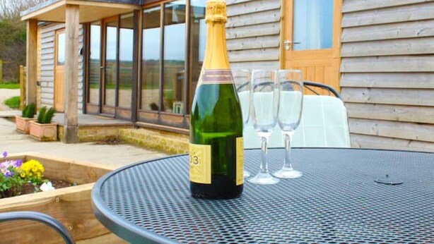 Champagnepaal op een tafel met twee glazen, buiten gezet voor een houten huis met grote ramen.