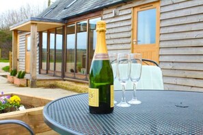 Champagnepaal op een tafel met twee glazen, buiten gezet voor een houten huis met grote ramen.