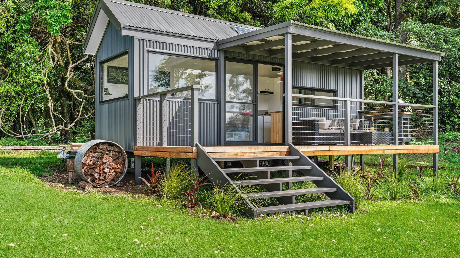 A modern, compact house with a deck, large windows, and a staircase leading to the entrance.