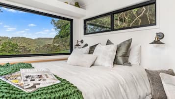 A bedroom with a large window, a bed with a green blanket, and a magazine on the bed.