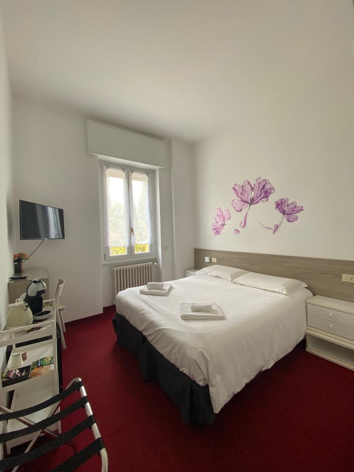 Une chambre d’hôtel avec un lit, un bureau et une chaise, une télévision et une fenêtre avec des rideaux.