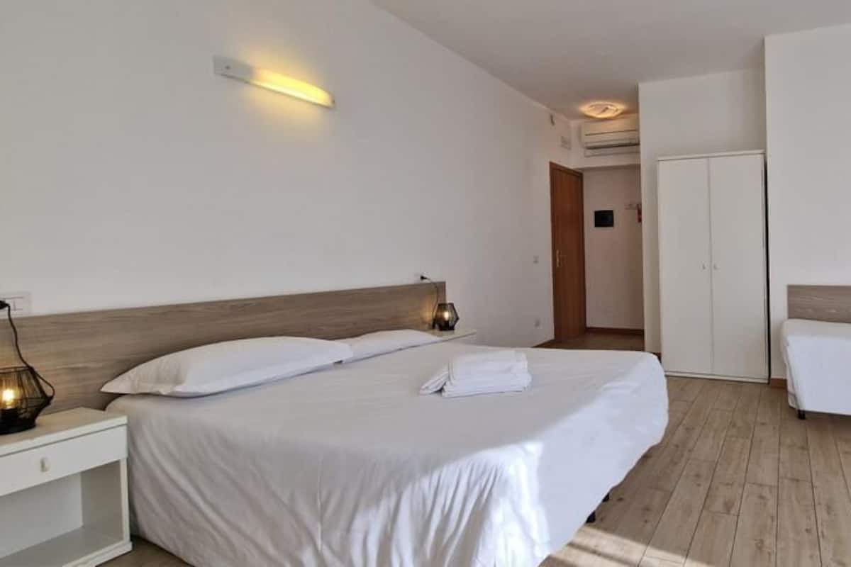 A hotel room with two beds, a wardrobe, and a bedside table with a lamp.