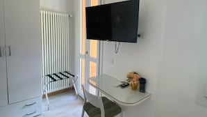 Una habitación moderna con televisión montada en la pared, una mesa de vidrio, una silla, un radiador y un armario.