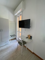 A modern room with a TV mounted on the wall, a glass table, a chair, a radiator, and a wardrobe.