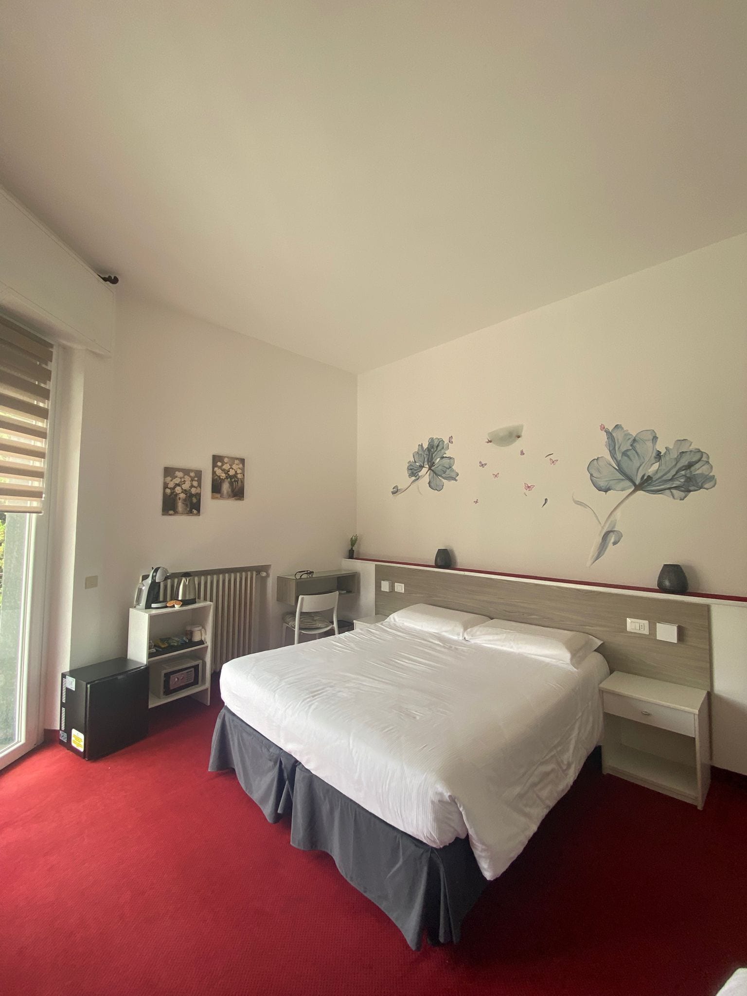 Une chambre d’hôtel équipée d’un lit, d’un bureau, d’une chaise, d’un radiateur et décorée avec des œuvres d’art mural.