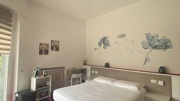 Een hotelkamer met een bed, een bureau, een stoel, een radiator en wanddecoratie.