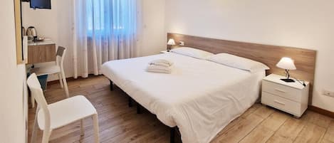 A hotel room with a bed, bedside tables, a desk, a chair, and a TV.