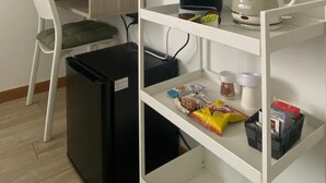 Una habitación compacta con escritorio, silla, televisión, estanterías y un cubo de basura.