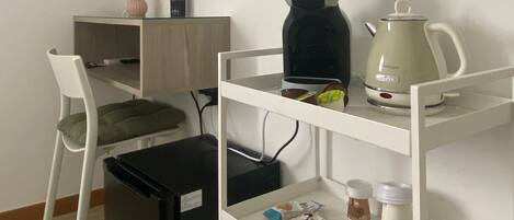 A compact room with a desk, chair, TV, shelves, and a trash bin.