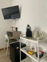 Una habitación compacta con escritorio, silla, televisión, estanterías y un cubo de basura.