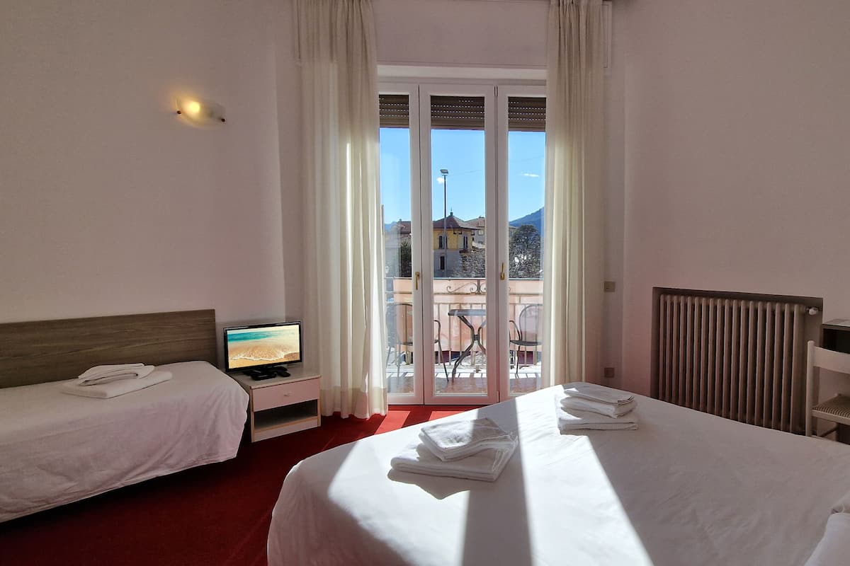 A hotel room with two beds, a TV, a desk with a kettle, and a view of the city through the window.