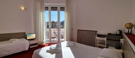 A hotel room with two beds, a TV, a desk with a kettle, and a view of the city through the window.