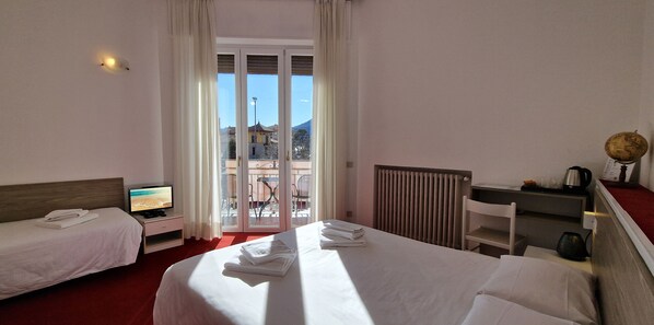 Habitación de hotel con dos camas, televisión, escritorio con hervidor y vista a la ciudad por la ventana.