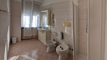 Een badkamer met toilet, bidet, wastafel en spiegel.