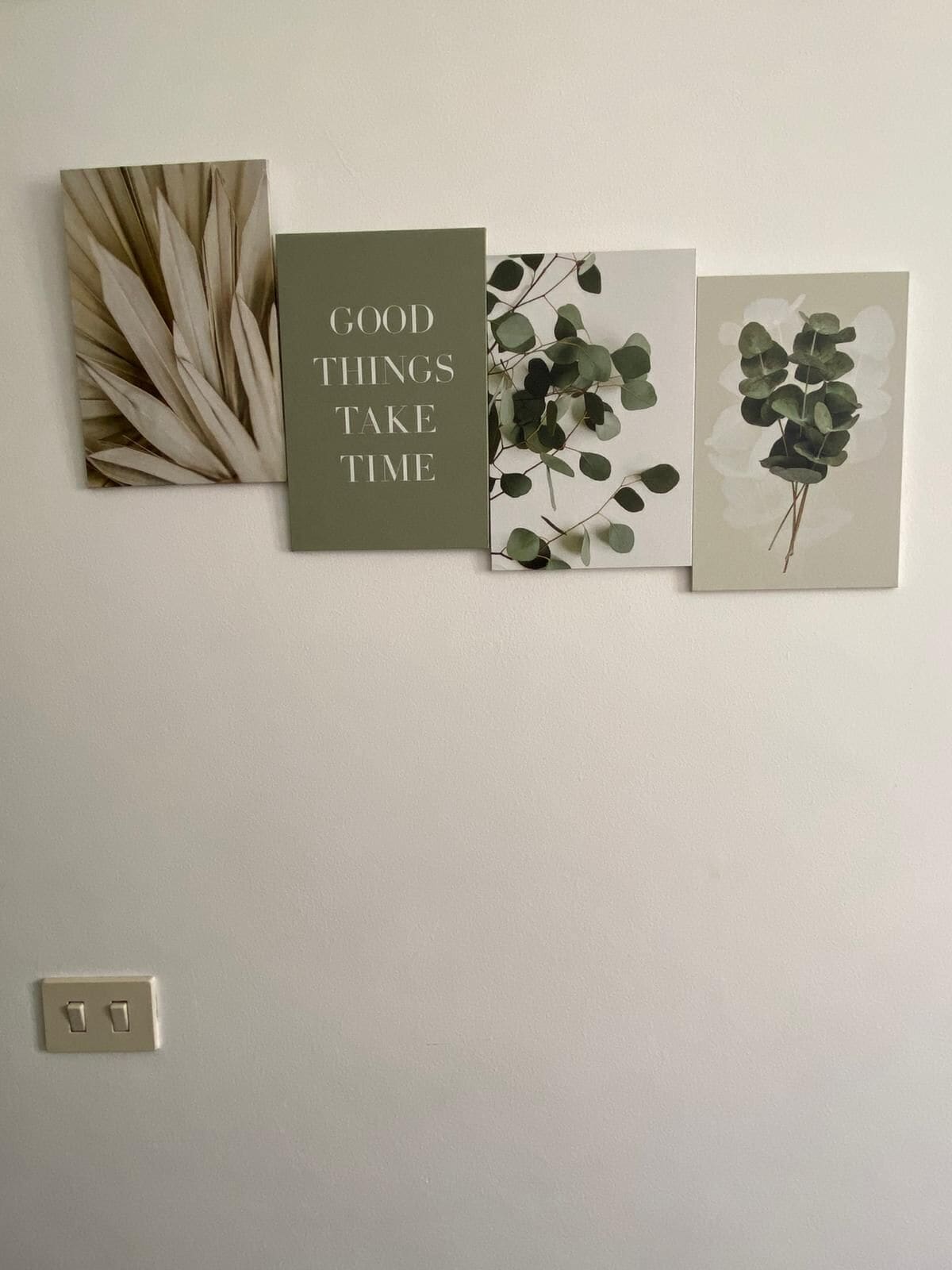 Una pared con cuatro cuadros enmarcados, uno con texto y tres con follaje.