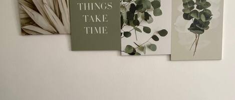 A wall with four framed artworks, one with text and three with foliage.