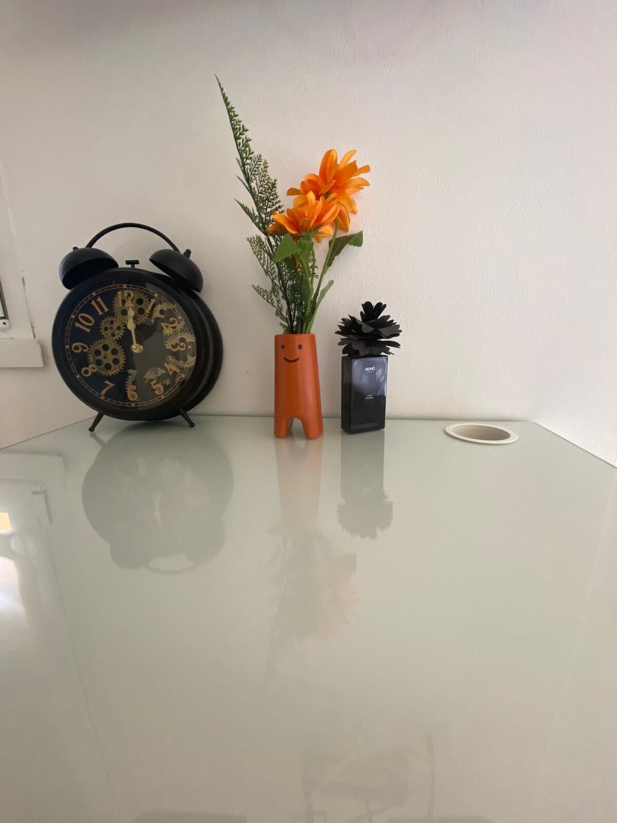 Une table avec une horloge, un vase à fleurs et une petite plante en pot.