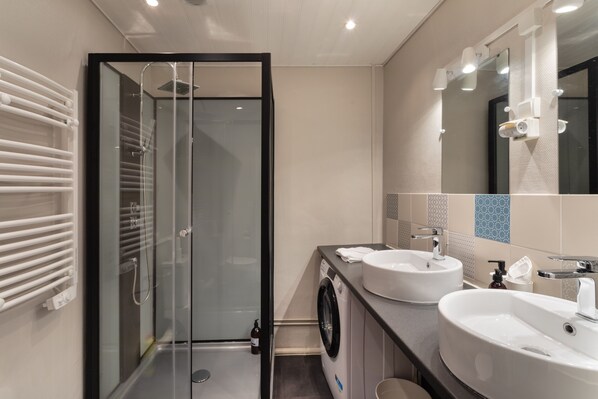 Un baño moderno con cabina de ducha de vidrio, lavamanos dobles y lavadora integrada.