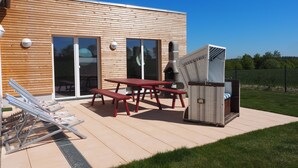 Un patio moderno al aire libre con terraza de madera, mesa de picnic roja y una parrilla integrada.