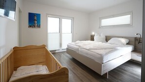 Un dormitorio con una cuna de madera, una cama doble y un ventanal grande.