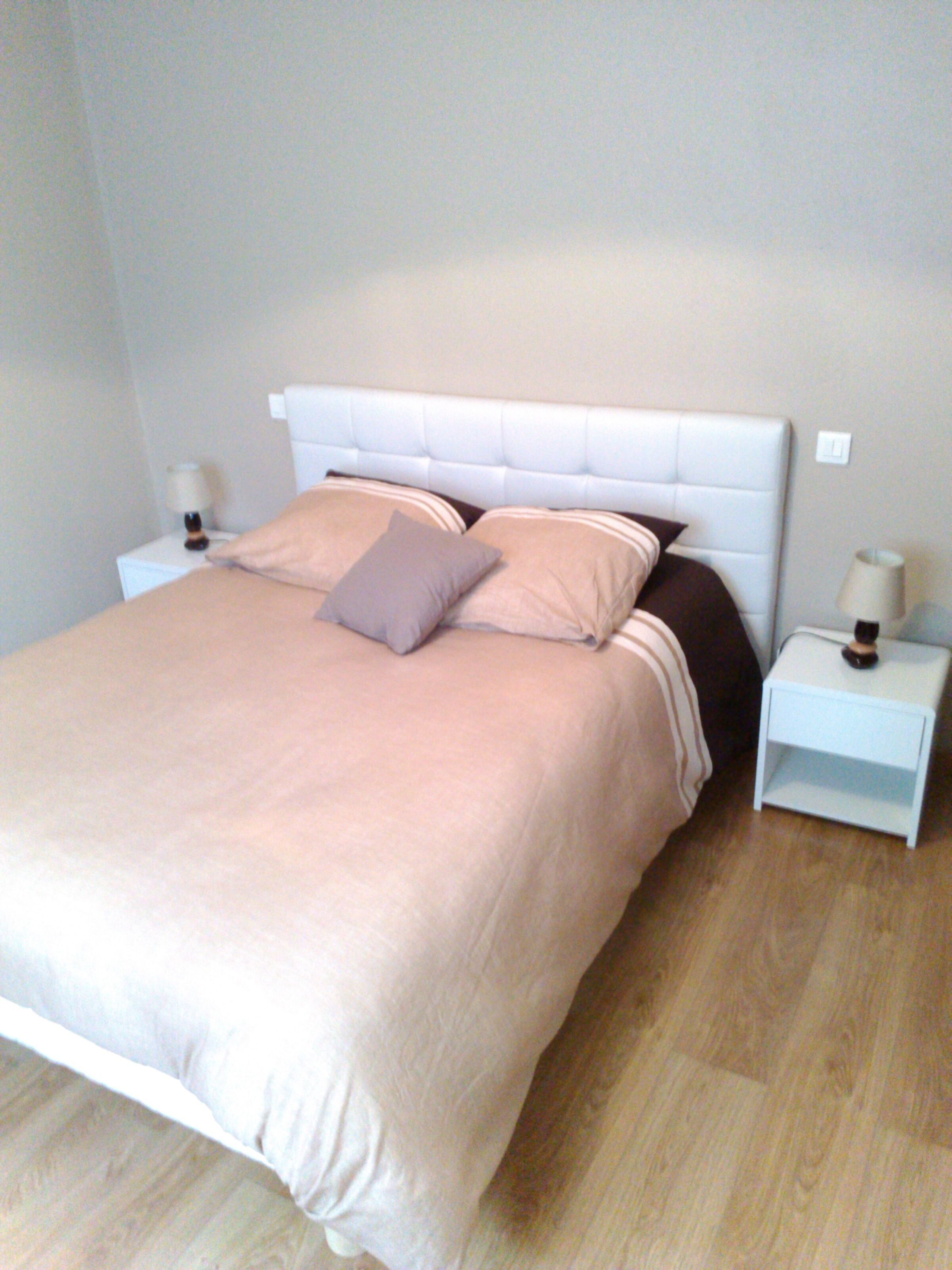 A neatly made bed with a headboard, two bedside tables with lamps, and a wooden floor.
