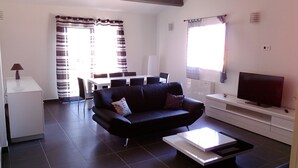 A modern living room with a black sofa, a coffee table, a TV, and a dining area with chairs and a table. - T3 - First floor - With swimming pool - Rated 5 * furnished for tourism (Piana)