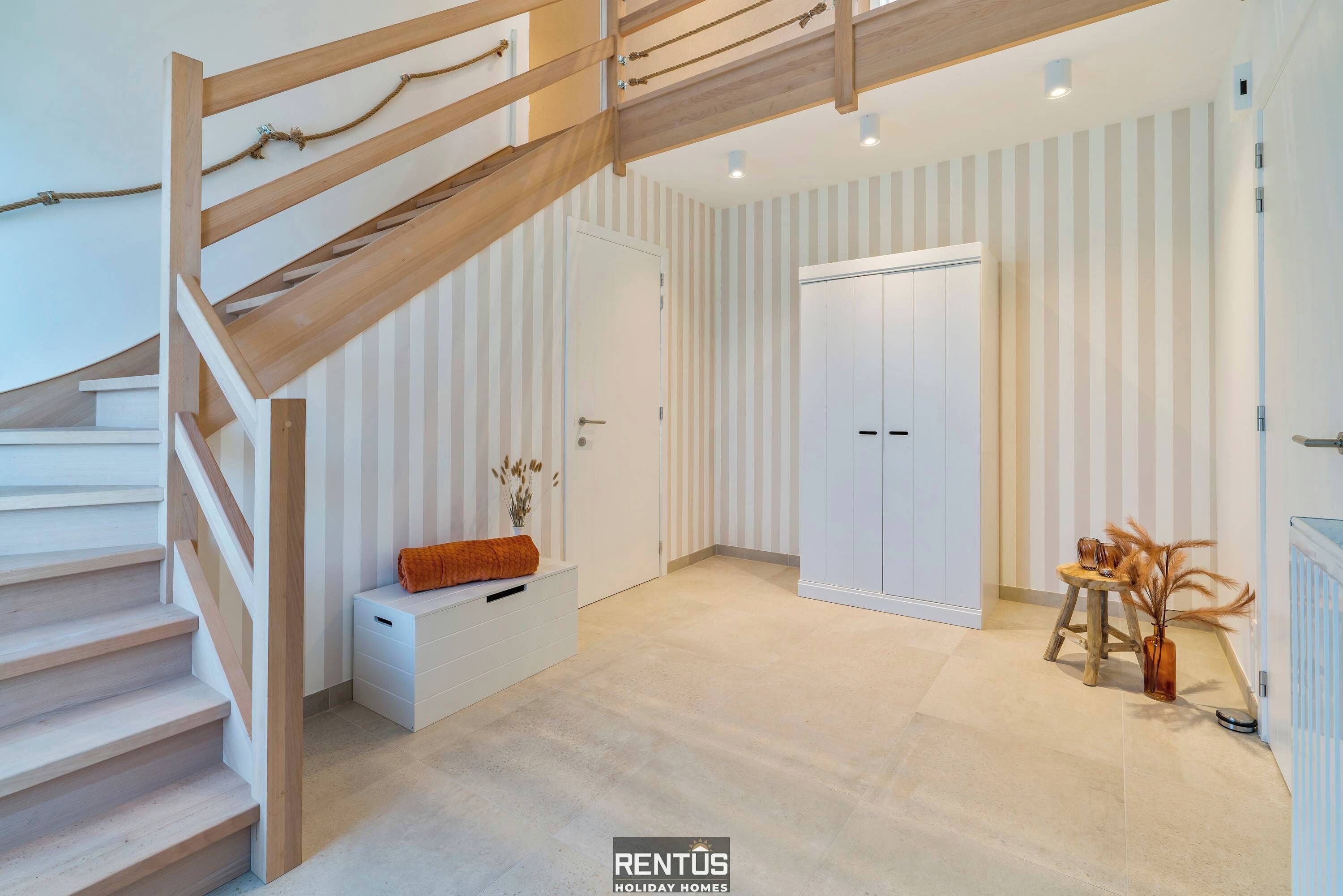 A modern interior with a wooden staircase, a white bench, a door, and a small table with decorative items.