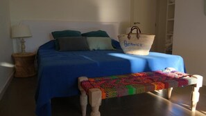 Relax in this serene bedroom with a large bed, woven basket, and colorful bench.