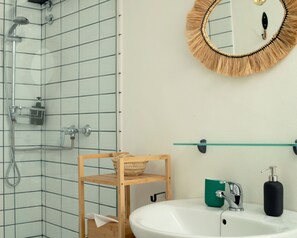 Bathroom features a grid-patterned tiled wall, a wooden shelf, and a round mirror with fringe border.