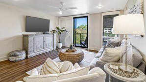 A modern living room with a flat-screen TV, a ceiling fan, a large window with a view, a sofa, and a coffee table.