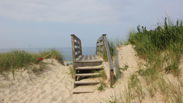 A wooden staircase leading to a sandy beach area with grass on either side. - 183 #3 N. Shore Blvd (Sandwich)